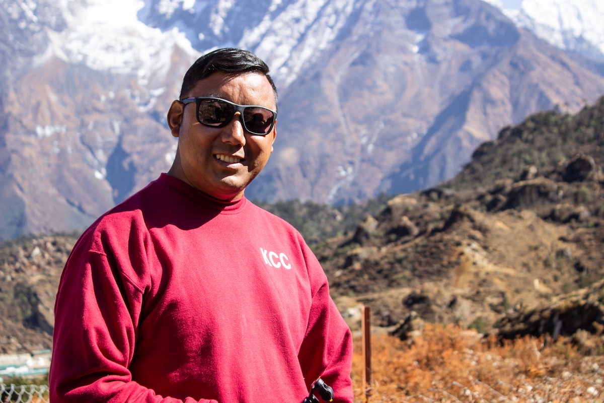 a stunning mountainous landscape, with snow-capped peaks and a man smiling at the camera